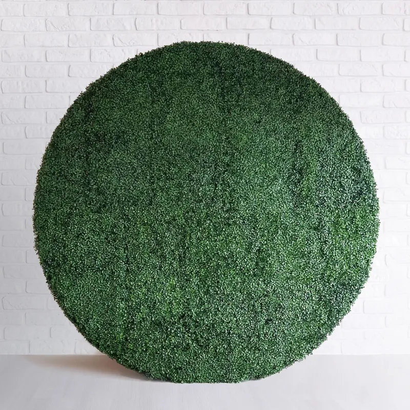 Circular Boxwood Backdrop, a large round artificial green hedge, against a white brick wall on a light floor