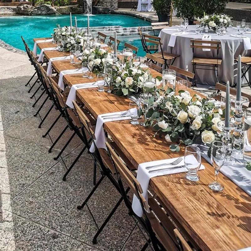 French Farm Tables set for an outdoor event beside a swimming pool, with white flowers, greenery and place settings