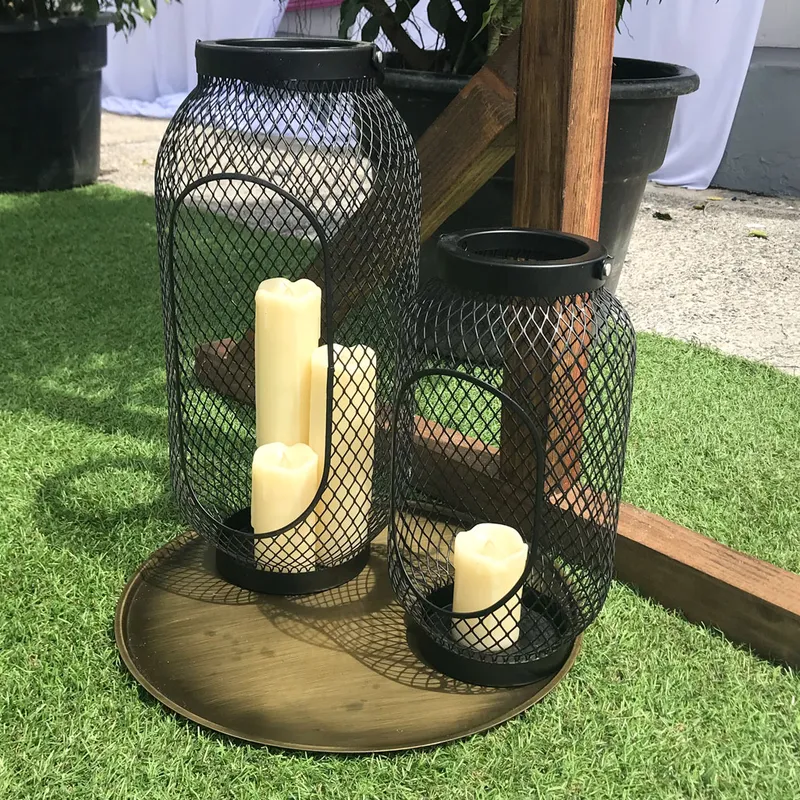 Three cream-coloured Candle Lanterns rest on a round brass tray on artificial grass
