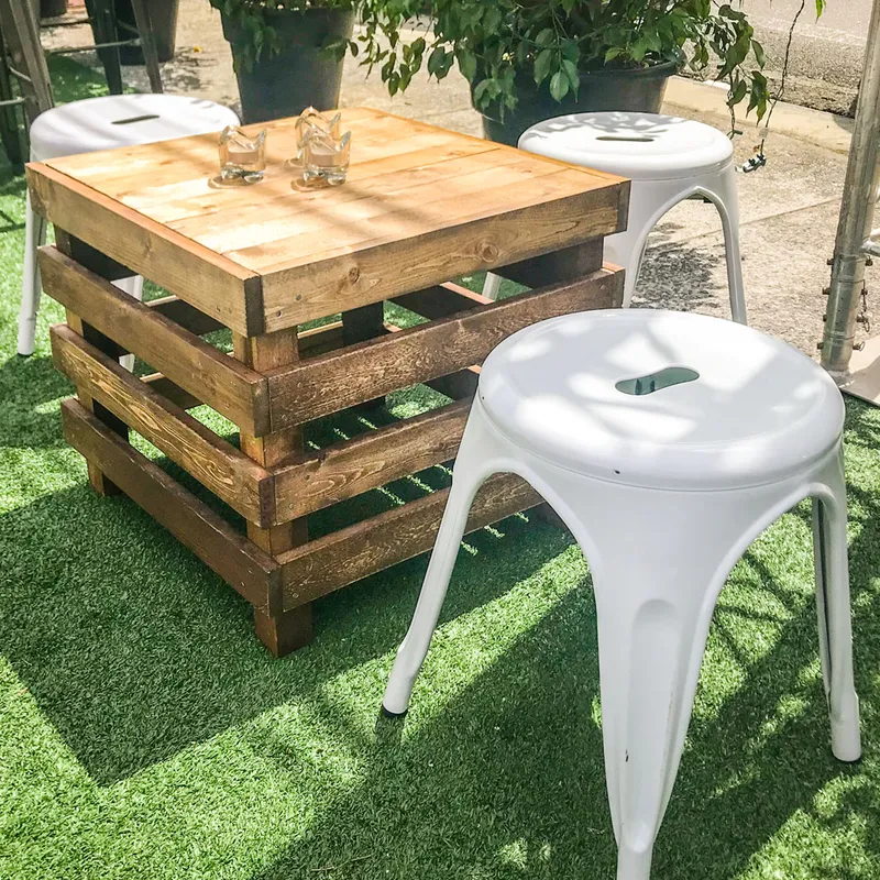 A Pallet Box with two glass tumblers, surrounded by white metal stools on artificial green grass in an outdoor set-up