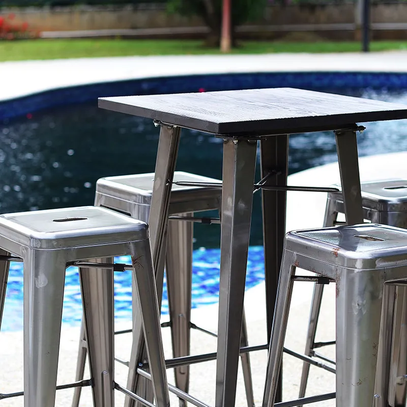 An Industrial Cocktail Table with four matching bar stools beside a swimming pool, with water visible behind