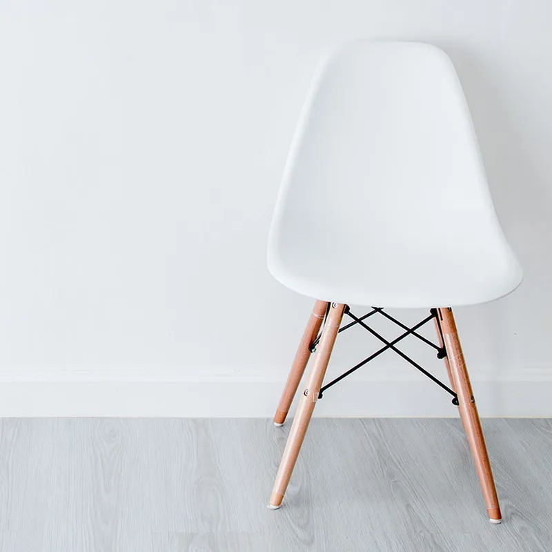 Eames Chair with a white plastic seat and wooden legs on a light grey wood floor against a plain white wall