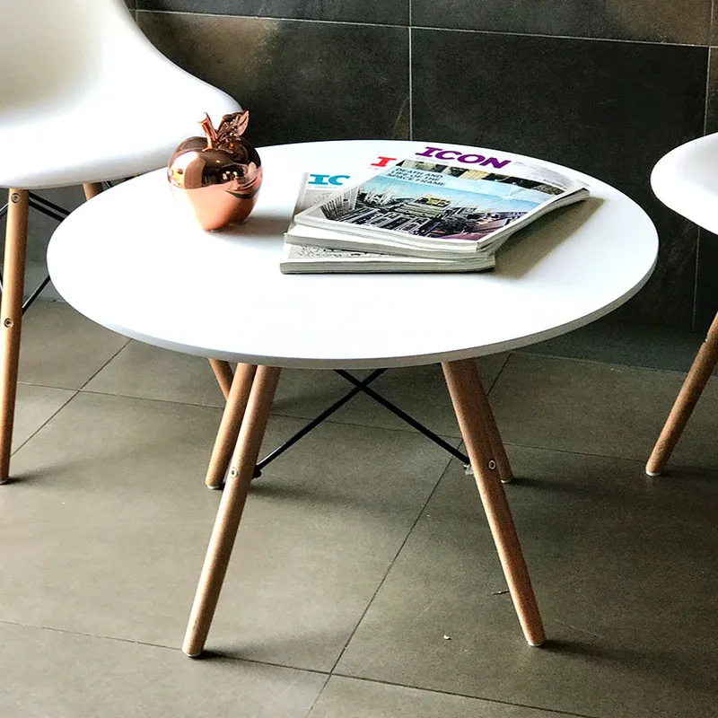 Eames Coffee Table, a white round table with wooden legs, holding a magazine and a small apple, beside two white chairs