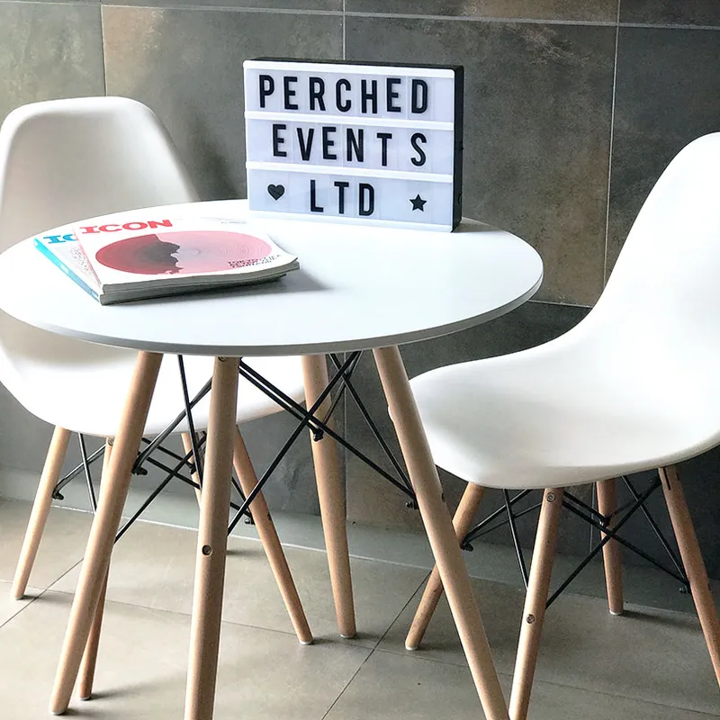 Eames Table, a small round table with two white chairs, magazines on the table and a sign reading PERCHED EVENTS LTD behind