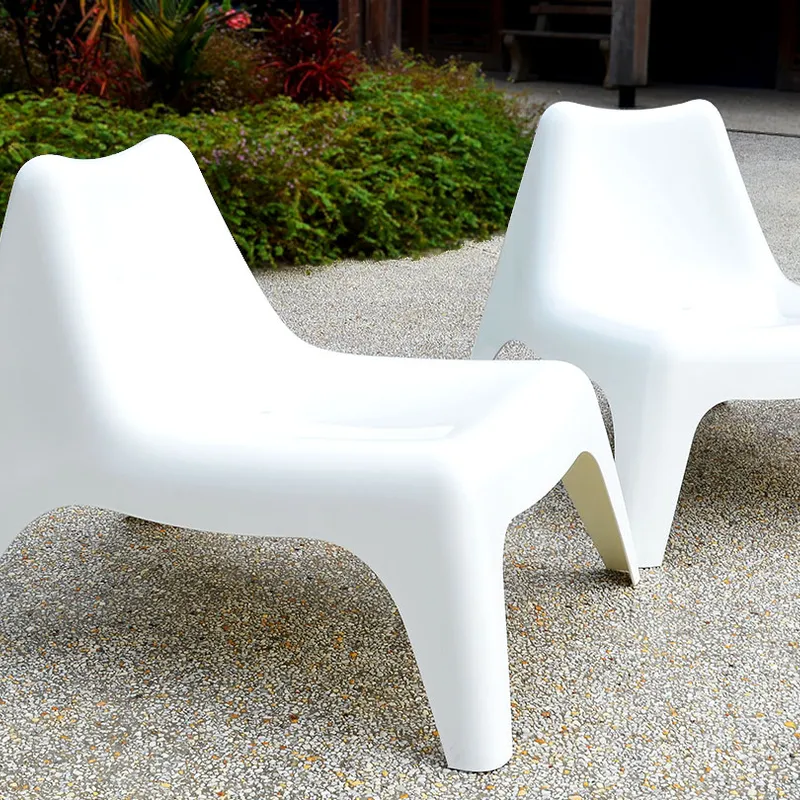 Two Poolside Easy Chairs, modern and white, on a gravel patio surrounded by green plants, with a building behind
