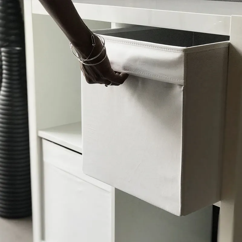 A hand pulls a Simple Storage Cube out of a white shelving unit, with two tall ribbed black vases in the background