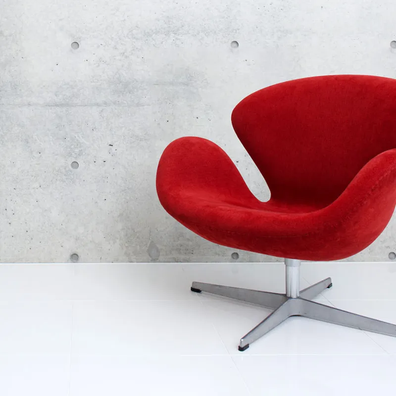 Swan Chair with a red upholstered seat, curved design and metal base, on a white floor against a grey concrete wall