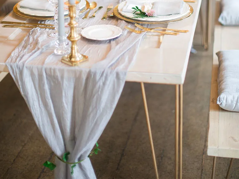 Hairpin Picnic Table set with gold cutlery, white plates and a floral centrepiece, with a cushioned wooden bench beside it