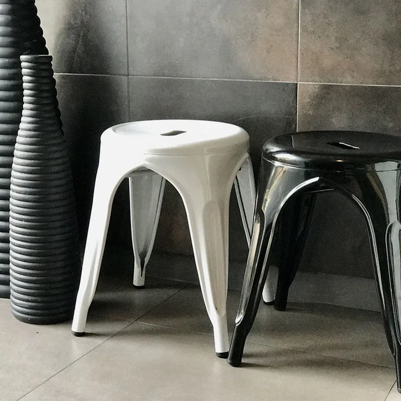 Two Industrial Stools, one white and one black, side by side next to three tall, ribbed vases against a tiled wall