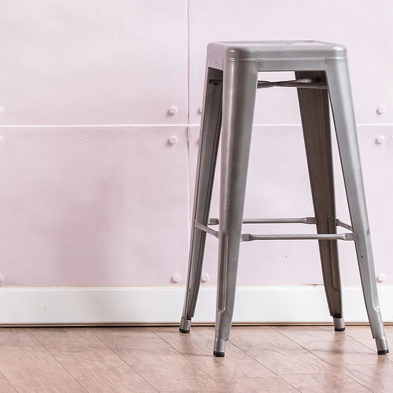 An Industrial Bar Stool sits on a wooden floor in front of a light pink, riveted wall