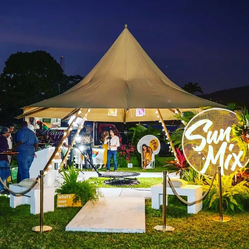 Tipi Tent with a pointed roof, lit at night for an event, with decorative plants and people gathered around it
